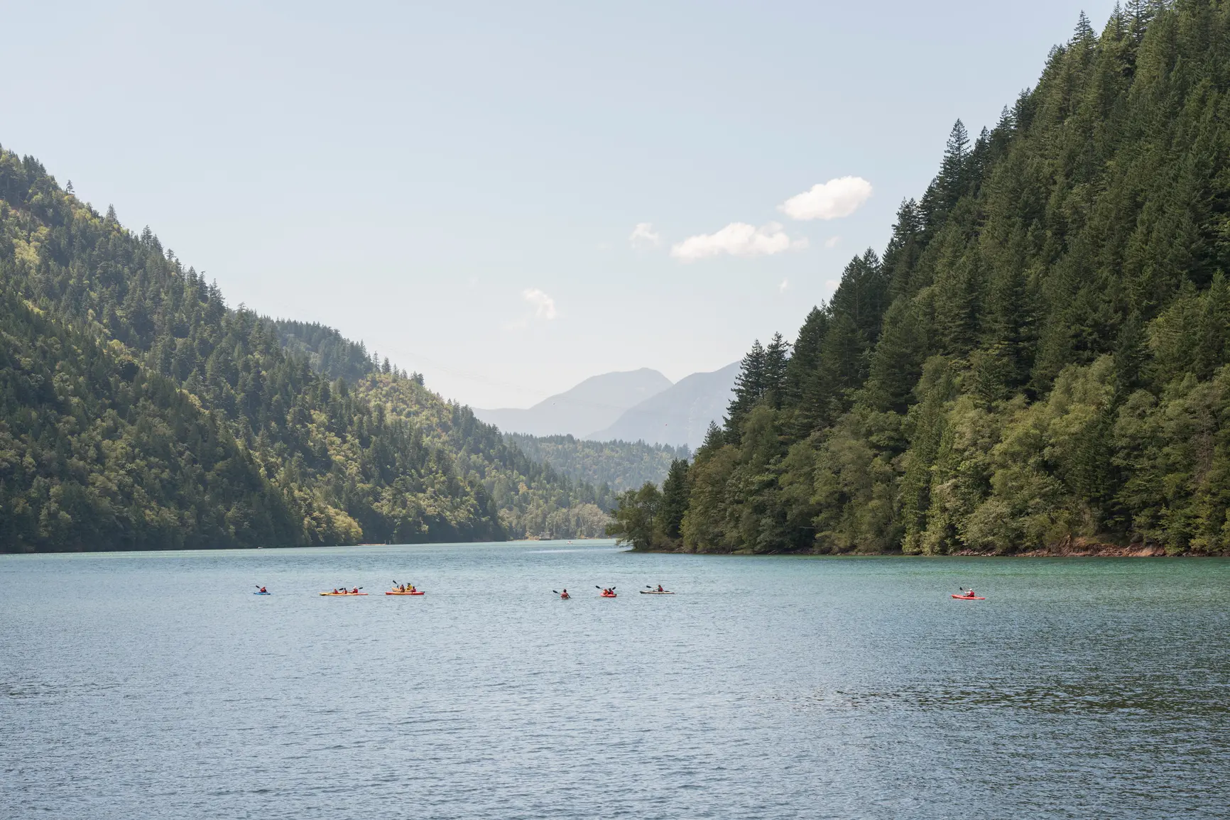 group of kayakers going on an adventure on a lake nestled between forested mountains on a nice summer's day